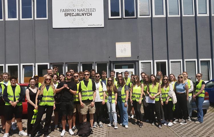 Grupowe zdjęcie na tle budynku studentów będących z wizytą w Fabryce Narzędzi Specjalnych