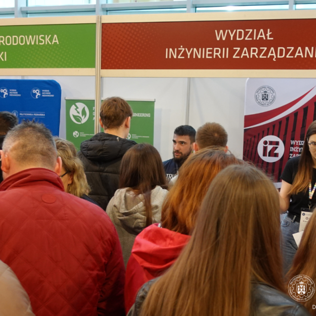 grupa uczniów tłocząca się na tle stanowisk poszczególnych wydziałow